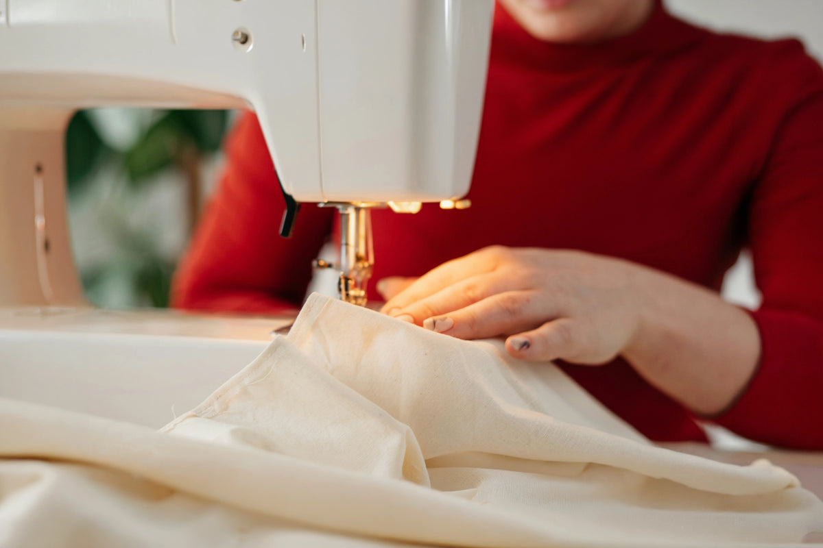 Manos guiando una tela clara bajo la aguja de una máquina de coser.